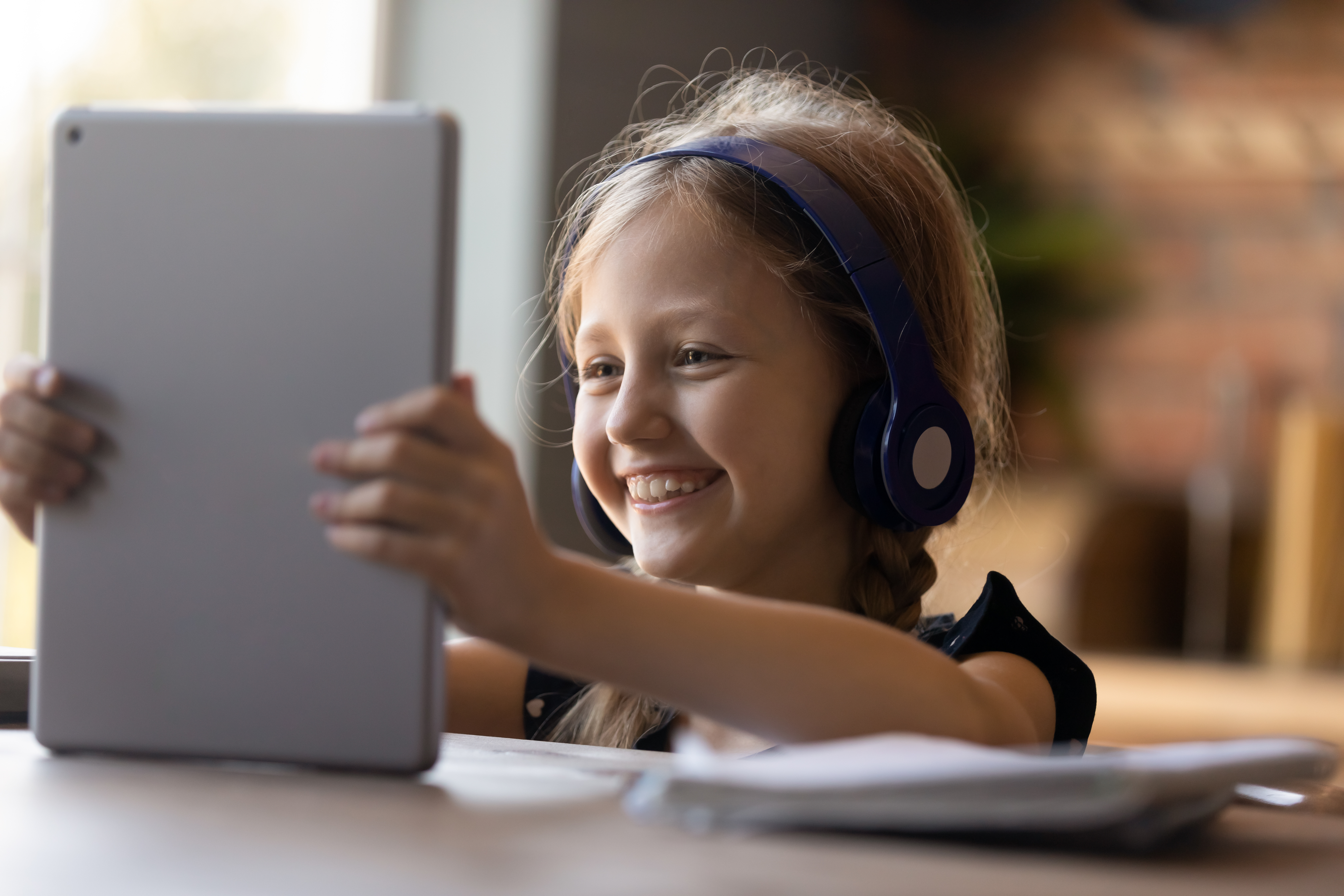 A child wearing headphones smiles as they use a tablet computer at a table